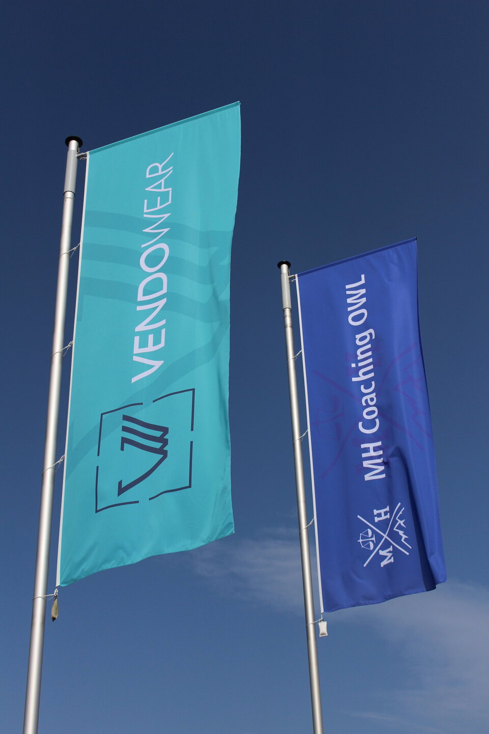 schicke Firmen-Werbung mit Hochformat-Ausleger-Fahnen
Vendowear in türkis, MH Coaching OWL in kräftigem Blau