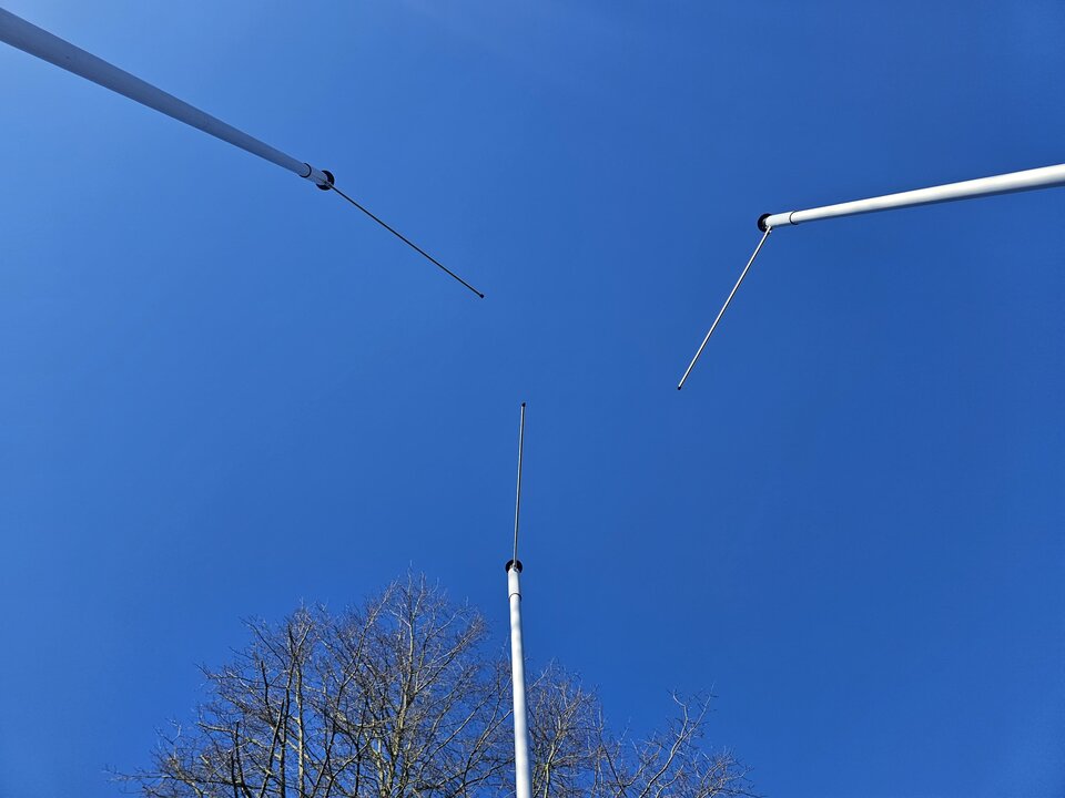 drei Ausleger-Fahnenmasten im Dreieck platziert, Blick von unten Richtung Ausleger und Himmel